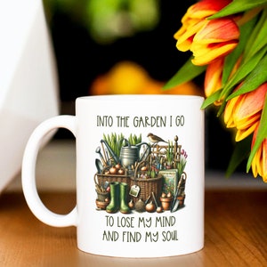 May include: White ceramic mug with a green, brown, and yellow illustration of gardening tools and the text "Into the garden I go to lose my mind and find my soul."