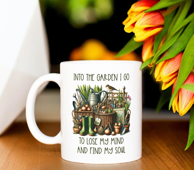 May include: White ceramic mug with a green, brown, and yellow illustration of gardening tools and the text "Into the garden I go to lose my mind and find my soul."