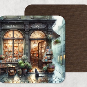 May include: A square coaster featuring a watercolor illustration of a quaint bookstore with arched windows and a black cat. The shop's name is "AISCE" and "AS €". The background is a cobblestone street and a brown leather-like coaster.
