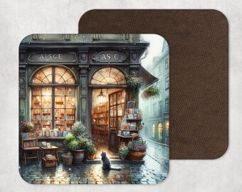 May include: A square coaster featuring a watercolor illustration of a quaint bookstore with arched windows and a black cat. The shop's name is "AISCE" and "AS €". The background is a cobblestone street and a brown leather-like coaster.