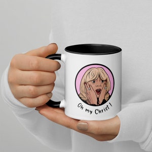 May include: White ceramic mug with a black interior and handle. The mug features a cartoon illustration of a surprised woman with the text "Oh my Christ!" in a black font. The woman has blonde hair and is framed by a pink circle.