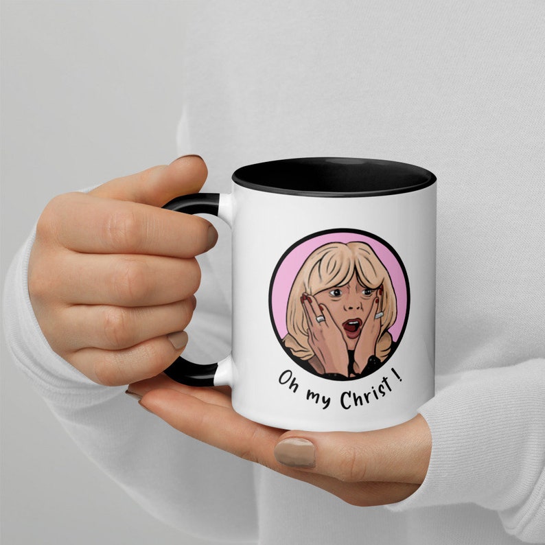 May include: White ceramic mug with a black interior and handle. The mug features a cartoon illustration of a surprised woman with the text "Oh my Christ!" in a black font. The woman has blonde hair and is framed by a pink circle.