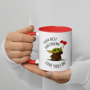 May include: White ceramic mug with a red rim. The mug features a cartoon image of a green alien character holding two red heart-shaped balloons. The text on the mug reads "Yoda Best Girlfriend Love You I Do."