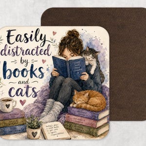 May include: Square coaster with a watercolor illustration of a person reading a book with two cats. The text reads "Easily distracted by books and cats." A cup of coffee and a notepad are also visible.