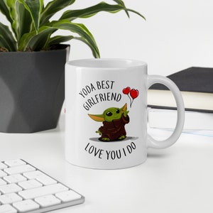 May include: White ceramic mug with a green cartoon character holding two red heart balloons. The text on the mug reads "Yoda Best Girlfriend Love You I Do."