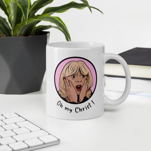 May include: White ceramic mug featuring a cartoon illustration of a surprised woman with blonde hair, red nails, and the text "Oh my Christ!" in black. The design is set within a pink circle.