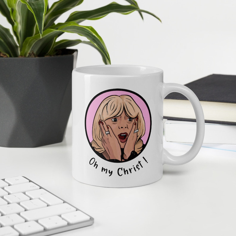 May include: White ceramic mug featuring a cartoon illustration of a surprised woman with blonde hair, red nails, and the text "Oh my Christ!" in black. The design is set within a pink circle.