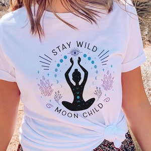 May include: White t-shirt with a graphic design of a woman in a yoga pose with the text "Stay Wild & Moon Child".