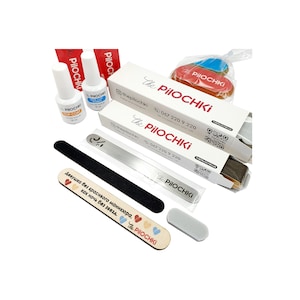 May include: A set of nail care products in a white box with the text "The Pilochki" and a phone number. The set includes a nail file, a nail buffer, a bottle of top coat, and a wooden stick with the text "Девушка без красивого маникюра, как ночь без звезд. The Pilochki".