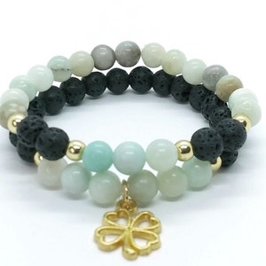 May include: Two beaded bracelets. One bracelet features black lava beads and light green beads, with gold-coloured accents. The other bracelet has a similar design, with a gold-coloured four-leaf clover charm.
