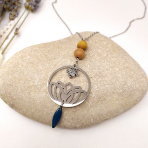 May include: A silver necklace with a circular pendant featuring a cutout design of leaves and a small knot charm. The necklace also includes two wooden beads in a light brown colour.