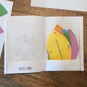 Puede incluir: Una actividad de desaf&iacute;o de lectura colorida con cinco formas de papel de diferentes colores. Cada forma tiene una pregunta escrita en ella. Las preguntas son: "&iquest;Cu&aacute;l es tu parte favorita de la historia?", "Yayi", "Voodoo", "T&iacute;tulo", y "Felicitaciones". La actividad se titula "Desaf&iacute;o de lectura".