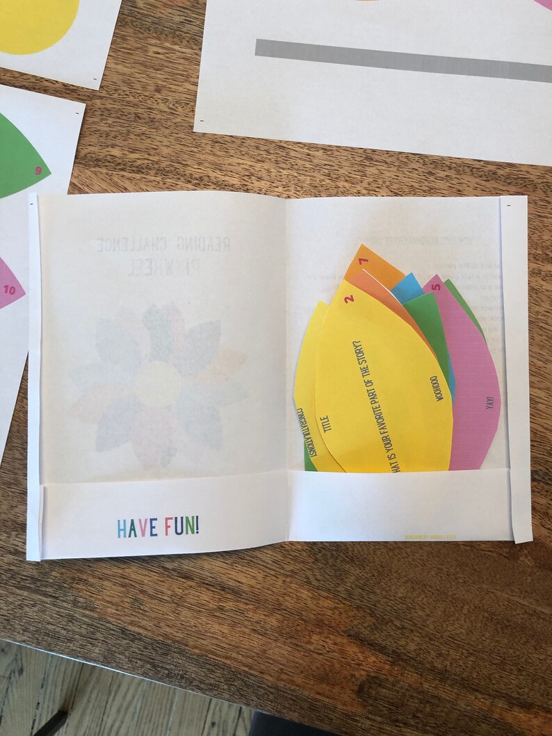 Puede incluir: Una actividad de desaf&iacute;o de lectura colorida con cinco formas de papel de diferentes colores. Cada forma tiene una pregunta escrita en ella. Las preguntas son: "&iquest;Cu&aacute;l es tu parte favorita de la historia?", "Yayi", "Voodoo", "T&iacute;tulo", y "Felicitaciones". La actividad se titula "Desaf&iacute;o de lectura".
