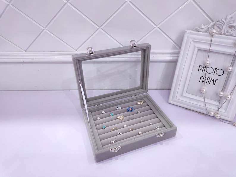 May include: A gray velvet jewelry box with a clear lid and multiple compartments for storing rings and earrings. The box has two silver clasps.