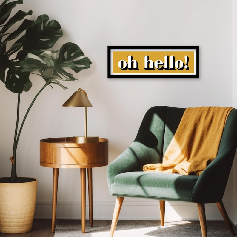 May include: A black framed print with a yellow background and the text "oh hello!" in white letters. The print is hanging on a white wall above a green armchair with a yellow throw blanket.