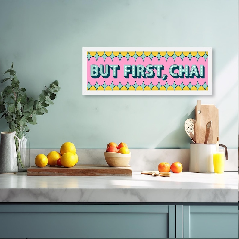 May include: A white framed print with a pink background and yellow and blue geometric shapes. The text "BUT FIRST, CHAI" is written in blue and white letters.