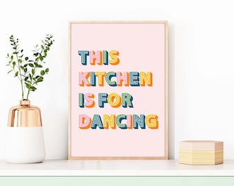 May include: A pink poster with the text "This Kitchen Is For Dancing" in colorful, 3D letters with white polka dots.
