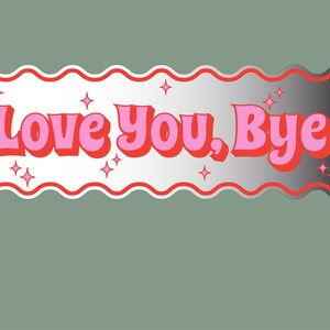 以下が含まれることがあります： 波状の白い縁と赤いアウトラインを持つ長方形のステッカー。「Love You, Bye」の文字はピンクと赤で、星のアクセントが付いています。背景はシルバーと黒のグラデーションで、くすんだ緑色の背景に配置されています。