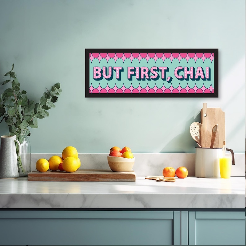 May include: A black framed sign with a pink and blue background and the text "BUT FIRST, CHAI" in pink letters. The sign is hanging on a light blue wall in a kitchen setting.