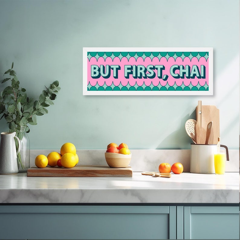 May include: A white framed print with a pink background and green and white geometric shapes. The text "BUT FIRST, CHAI" is written in pink letters with a white outline.