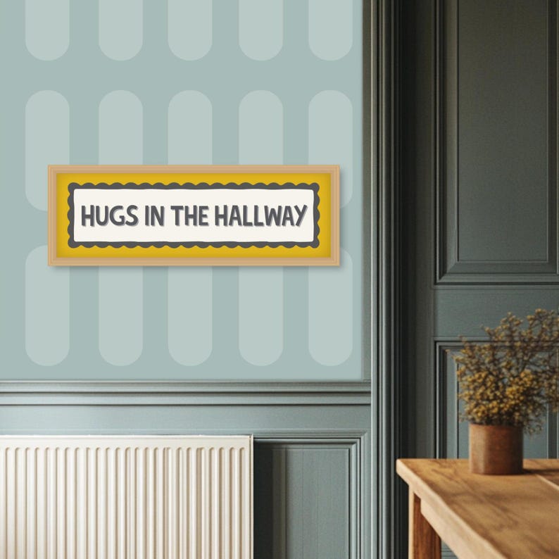 May include: A framed sign with the text "HUGS IN THE HALLWAY" in a black font. The sign has a yellow border and a scalloped edge. The sign is hanging on a light blue wall with a pattern of oval shapes.