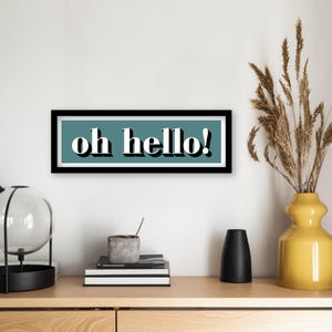 May include: A framed print with a teal background and white text that reads "oh hello!" The frame is black and has a white border.