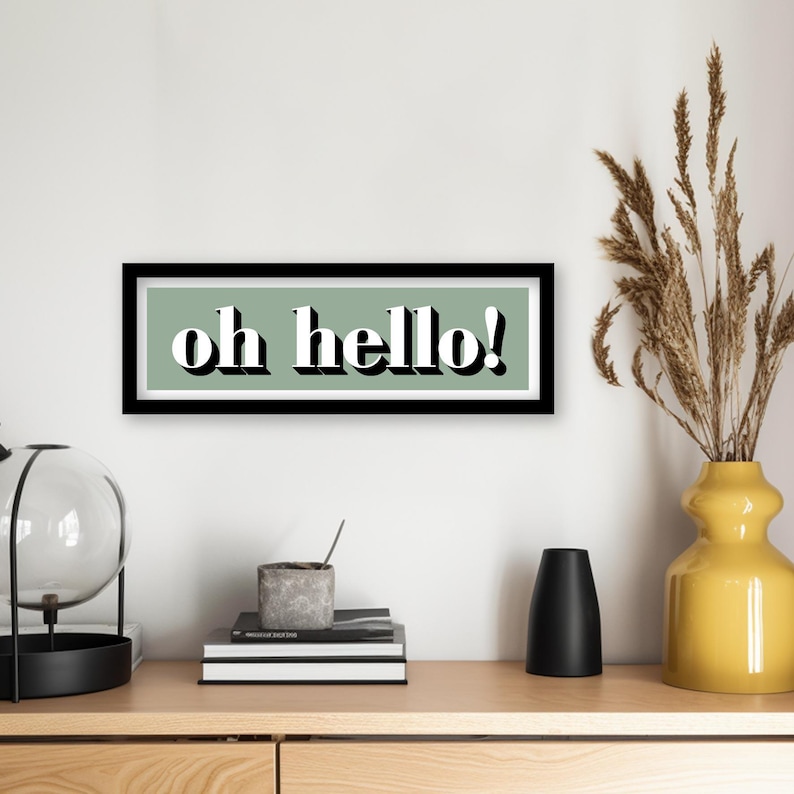 May include: A black framed print with a sage green background and white text that reads "oh hello!"
