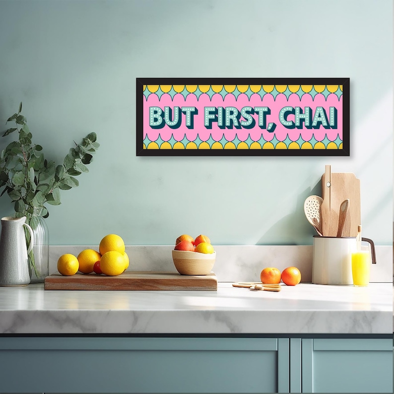 May include: A framed print with a pink background and a teal and yellow geometric pattern. The print reads "BUT FIRST, CHAI" in a bold, retro font.