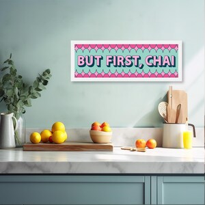 May include: A white framed print with a teal background and pink and white geometric shapes. The print says "BUT FIRST, CHAI" in pink letters.
