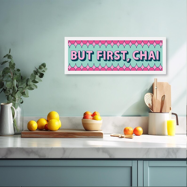 May include: A white framed print with a teal background and pink and white geometric shapes. The print says "BUT FIRST, CHAI" in pink letters.