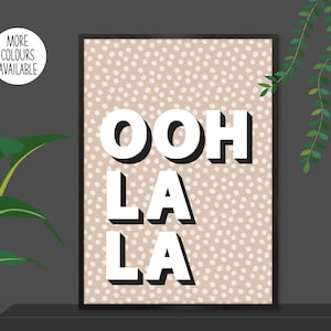 以下が含まれることがあります： ベージュと白のドット柄のプリントに、白で太字の3D文字で「ooh la la」と書いてあります。プリントは黒いフレームで囲まれています。