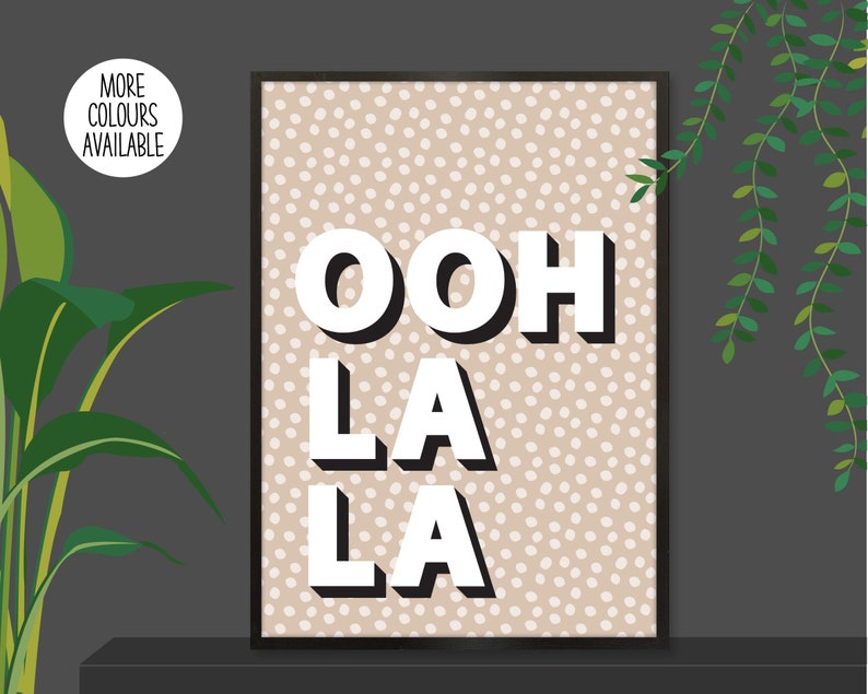 以下が含まれることがあります： ベージュと白のドット柄のプリントに、白で太字の3D文字で「ooh la la」と書いてあります。プリントは黒いフレームで囲まれています。