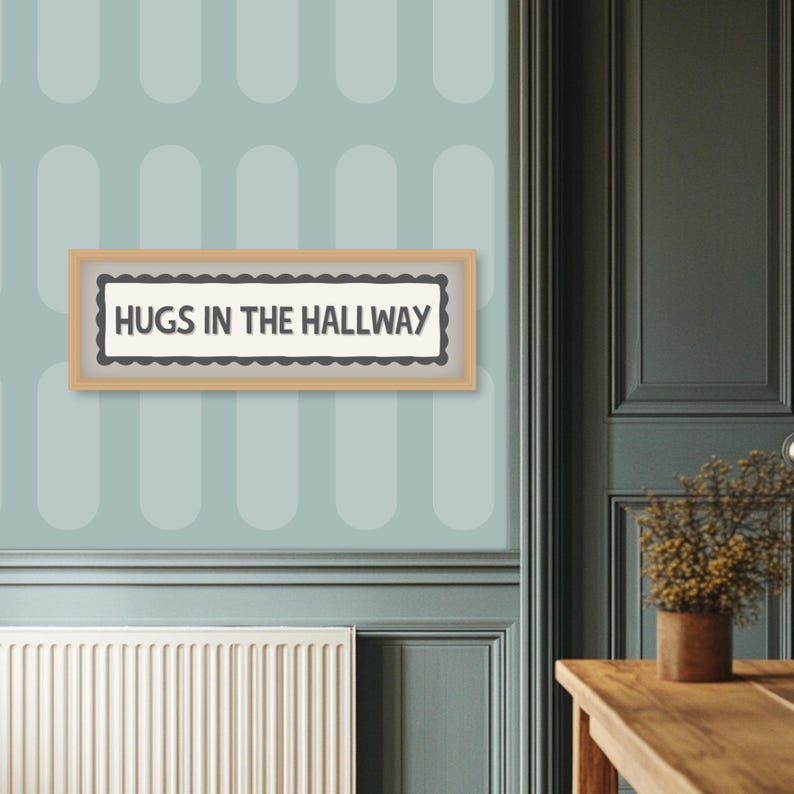 May include: A rectangular wooden framed sign with the text "HUGS IN THE HALLWAY" in a black font. The sign has a scalloped border and is mounted on a light blue wall with a repeating oval pattern.