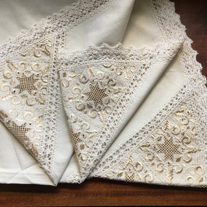 May include: Cream tablecloth with gold embroidery and lace trim. The design features a central star motif and floral patterns. The tablecloth is folded, revealing the detailed craftsmanship. The measurements are in centimeters.