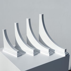 May include: Four white corner brackets of varying sizes, arranged in a row from smallest to largest. The brackets are made of a smooth, white material and have a slightly curved shape.