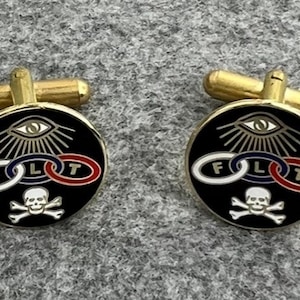 May include: A pair of gold cufflinks with a black enamel design. The design features an eye with rays of light, three interlocking rings with the letters F, L, and T, and a skull and crossbones.