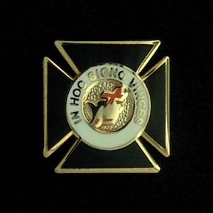 May include: A gold-coloured pin with a black enamel cross. The centre of the cross features a white circle with a red cross and the text "IN HOC SIGNO VINCES".