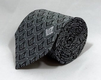May include: A gray silk tie with a black and white pattern of repeating Masonic symbols. The tie is rolled up and the pattern is visible on the roll.
