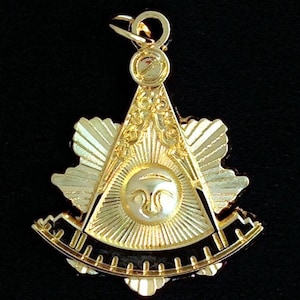 May include: A gold-colored Masonic pendant featuring a compass and square with a sun and eye design in the center.