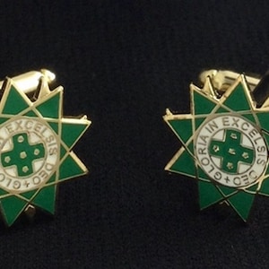 Könnte beinhalten: Ein Paar goldene Manschettenknöpfe mit einem grünen und weißen Emaille-Design. Das Design zeigt einen Stern mit einem Kreuz in der Mitte und dem Text "DEO GLORIA IN EXCELSIS".