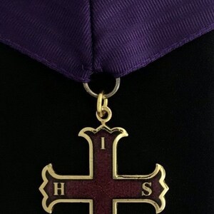 May include: A gold cross pendant with a purple ribbon. The cross has a burgundy center with the letters "IHS" and "V" in gold.