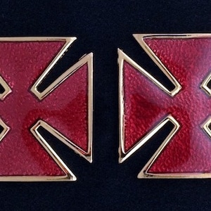 May include: Two red enamel crosses with gold trim. The crosses are symmetrical and have a simple design.