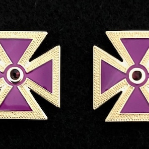 Könnte beinhalten: Ein Paar goldfarbene Manschettenknöpfe mit einem Kreuzdesign aus violettem Emaille und einem roten Juwel in der Mitte.