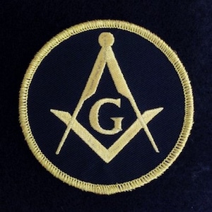 May include: A gold embroidered Masonic symbol patch on a dark blue background. The symbol is a square and compass with a 'G' in the centre.