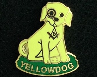 May include: A yellow dog pin with a black eye patch and a gold Masonic symbol on its chest. The dog is sitting on a green base with the word "YELLOWDOG" written in gold letters.