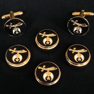 May include: A set of gold-toned cufflinks and shirt studs. The black enamel pieces feature a gold sword and crescent moon design with a star. The cufflinks have a gold bar backing. The shirt studs are round with a gold rim.