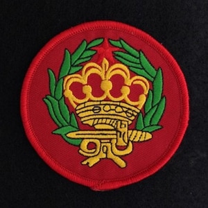 May include: A red circular patch with a gold crown, sword, and green laurel wreath. The crown has red jewels and the sword has a gold hilt.