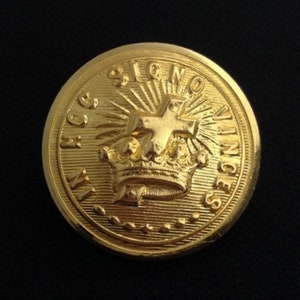 May include: A gold-colored button with the words "In Hoc Signo Vinces" and a crown with a cross above it.