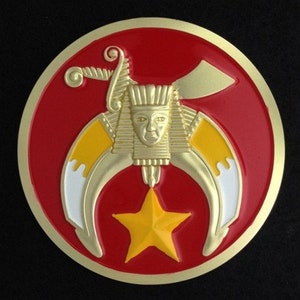 May include: A gold-coloured Masonic emblem with a red background. The emblem features a crescent moon with two points, a five-pointed star, and a stylised human head.