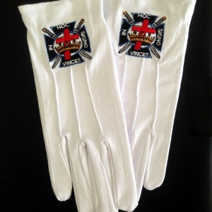 May include: A pair of white cotton gloves with embroidered insignia. The insignia features a red cross, a crown, and two swords with the text "In Hoc Signo Vinces".